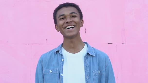 Fröhlicher afroamerikanischer Junge lacht auf rosa Hintergrund und genießt unbeschwerte Jugend — Stockvideo