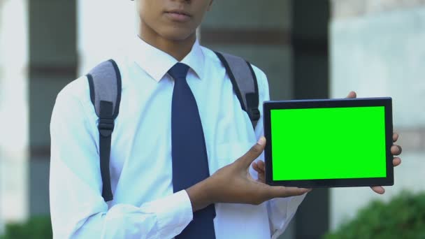 Okul çocuğu yeşil ekranlı tablet gösteriyor, kitap kitaplığı uygulamalarının reklamını yapıyor — Stok video