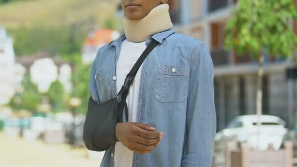 Upset teen boy wearing foam cervical collar and broken hand bandage, accident — Stock Video