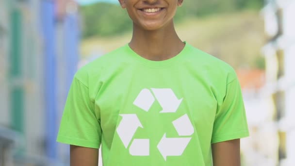 Niño en camisa con signo de reciclaje sonriendo en la cámara, la promoción de productos reutilizables — Vídeos de Stock