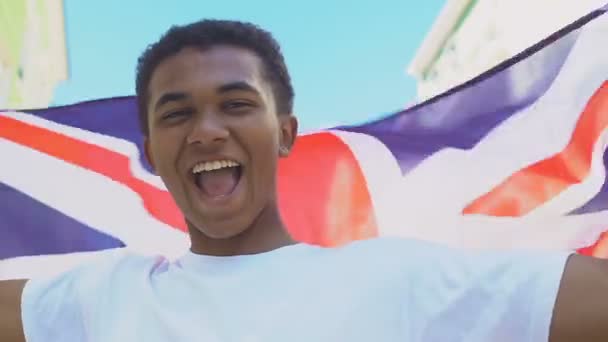 Extremely happy Afro-American male teenager waving British flag, festive mood — 图库视频影像