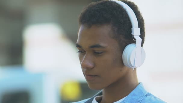 Bouleversé afro-américain adolescent garçon dans casque écoute de la musique mélancolique — Video