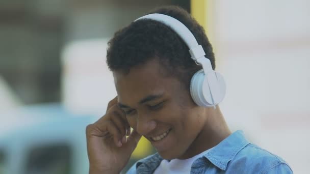 Afro-Amerikaanse mannelijke tiener in hoofdtelefoon bewegen in ritme van de muziek, stemming — Stockvideo