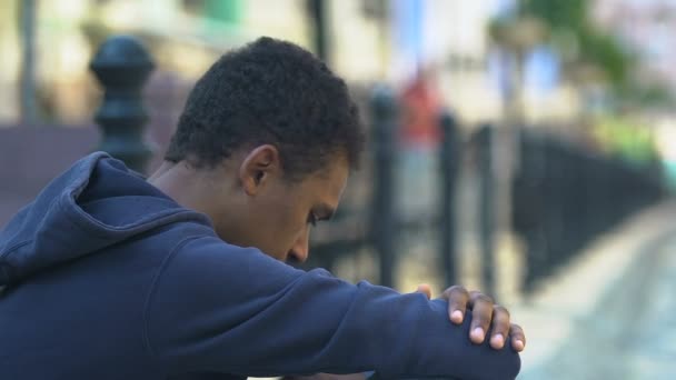 Upset African-American boy sitting alone outdoors, race discrimination victim — Stock Video