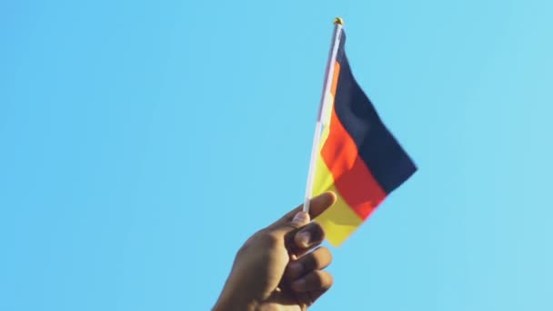 Mano del hombre negro sosteniendo la bandera alemana contra el fondo del cielo, día de la independencia — Vídeo de stock