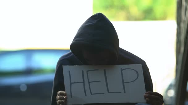 Hooded black male refugee showing cardboard with help word, needing shelter — Stock Video