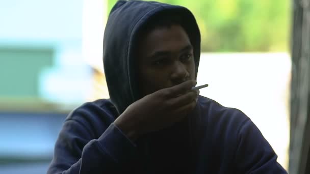 Afro-Amerikalı genç çocuk sigara içiyor, sigara içtikten sonra öksürüyor, kötü alışkanlık. — Stok video