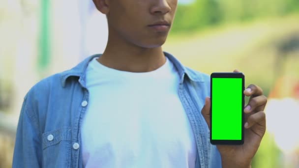 Adolescente masculino negro serio señalando el dedo en el teléfono inteligente con pantalla verde — Vídeos de Stock