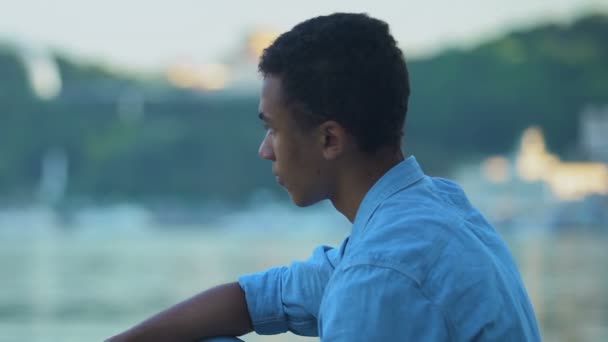 African-American teen boy throwing stones in city lake, relaxing outdoors — стокове відео