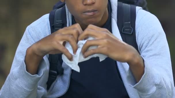 Sad mixed-race male teen with rucksack eating sandwich alone, depression — Stock Video