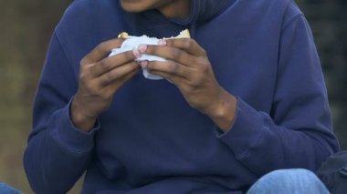 Aç Afro-Amerikalı genç erkek aç gözlülükle sandviç yiyor, fakirlik...