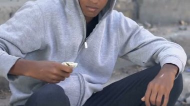Bunalımlı, yalnız, Afro-Amerikan kapüşonlu genç. Dolarlara bakıyor.