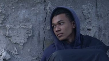 Kapüşonlu Afro-Amerikalı erkek mülteci şehir caddesinde tek başına oturan, umutsuzluk