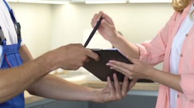 Kadın evrakları imzalıyor ve tamirden sonra erkek tesisatçıya geri veriyor.