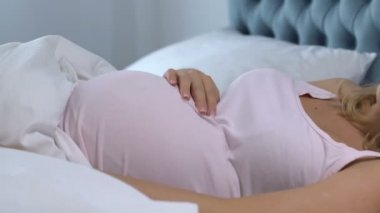 Yatakta yatan, yastıkla yüzünü kapatan, gürültülü komşulardan rahatsız olan hamile kadın