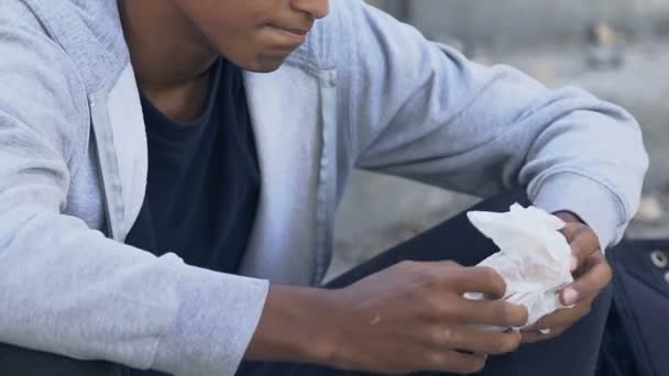 Smutny głodny czarny nastolatek mężczyzna jedzenie hamburger sam na ulicy, depresja — Wideo stockowe
