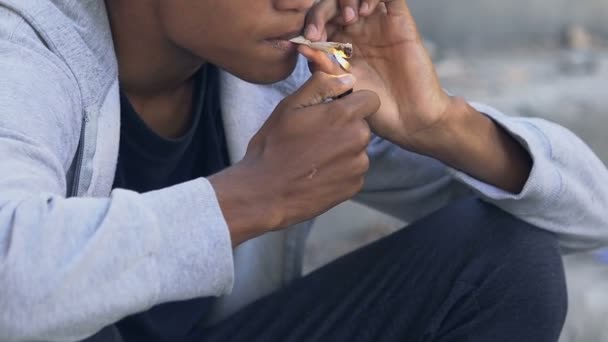 Νεαρός Αφρο-Αμερικανός εθισμένος αρσενικό κάπνισμα κοινό υπαίθριο, κακές συνήθειες και τα ναρκωτικά — Αρχείο Βίντεο
