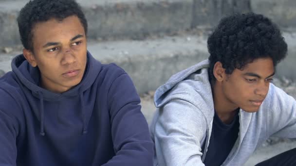 Depressed african american injured male teen friends sitting alone on street — Stock Video