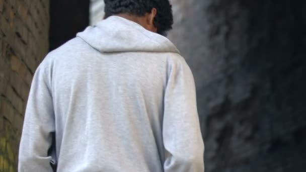 Одинокий афро-американец, прогуливающийся по заброшенному месту, оглядывающийся назад грустью — стоковое видео
