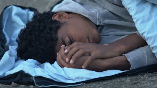 Замораживание афроамериканского беженца, лежащего на улице в спальном мешке, безнадежность — стоковое видео