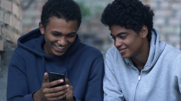 Black male teenager showing friend photos on smartphone, having fun outdoors — Stock Video