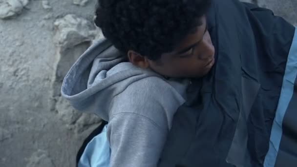 Black teen boy lying in sleeping bag on street, escape from home, problems — Stock Video