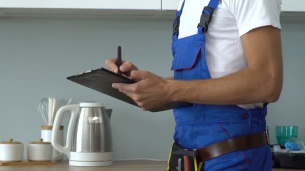 Guapo reparador de ropa de trabajo lista de escritura de trabajo hecho y mirando a cosas de la cámara — Vídeo de stock