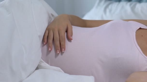 Беременная женщина лежит в постели и гладит животик, ждет ребенка, любит — стоковое видео