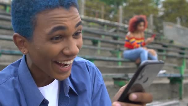 Lachen blauw-harige mannelijke student kijken grappige video op smartphone, app — Stockvideo