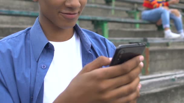 Ontspannen afro-Amerikaanse mannelijke tiener kijken prank video op mobiele telefoon en glimlachen — Stockvideo