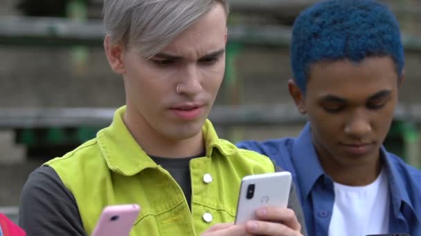 Blond hipster kille som visar ny app på mobiltelefon till multiracial vänner, prylar — Stockvideo