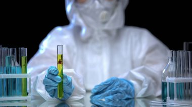 Laboratuvar çalışanı sarı sıvıyla test tüpü gösteriyor ve son derece yanıcı bir işaret.