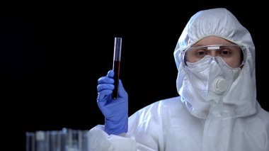 Koruyucu kıyafetli kadın araştırmacı test tüpünde yağ sıvısı gösteriyor, zehir.