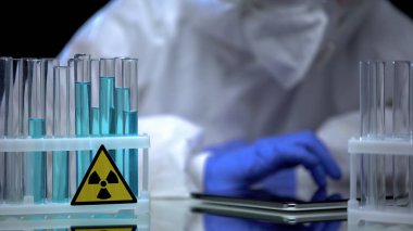 Test tüpünde mavi radyoaktif sıvıyı test eden eldivenli laboratuvar çalışanı, sekme üzerine notlar