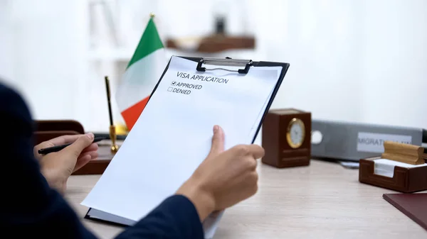 Embassy employee approving visa application, italian flag on table, government