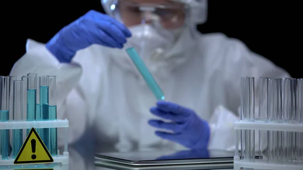 危険な液体管 テーブルの上のタブレットを分析保護スーツの科学者 — ストック写真
