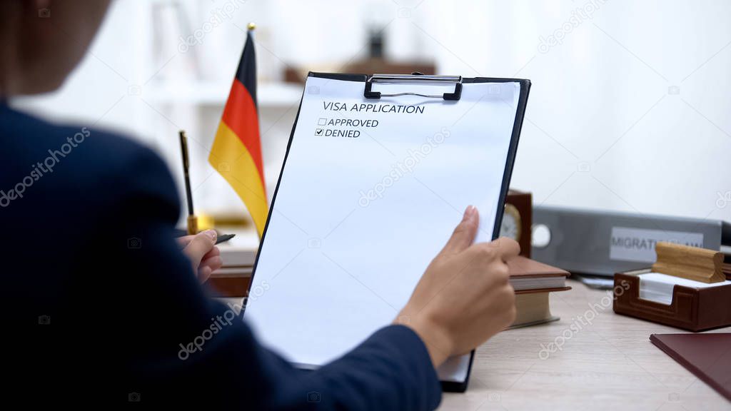 Immigration inspector denying visa application, german flag on table, embassy