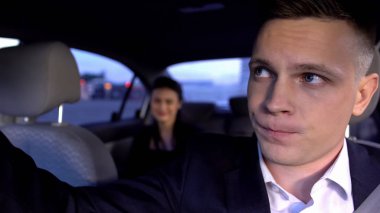 Şoför hoşnutsuz ve arabadaki müşteri ve kötü taksi servisinden rahatsız görünüyor.