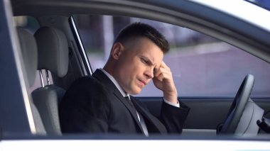 Upset man sitting in car, thinking over problems, stressful life, overwork