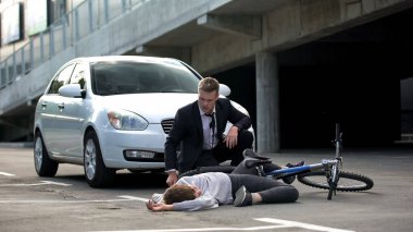 Genç sürücü baygın bir kazaya bakıyor. Kurban asfaltta yatıyor, yol tehlikesi var.