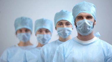 Professional surgeon team in mask and uniform looking at camera, hospital work clipart