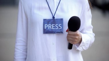 Basın kimliği olan kadın gazeteci mikrofon tutuyor, röportaj için hazırlanıyor.