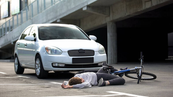 Unconscious bicyclist on asphalt street hit by car, traffic collision danger