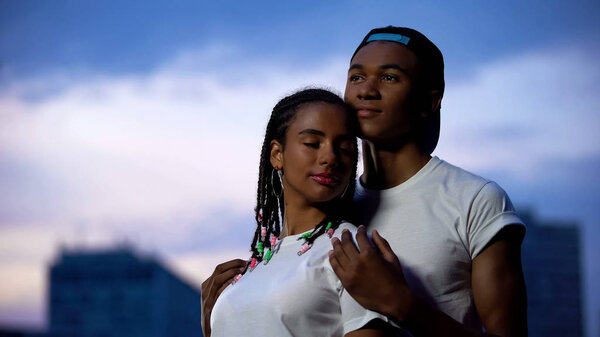 Afro-american couple embracing against evening sky, supportive relationships