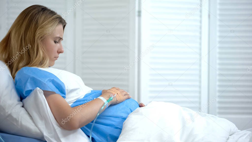 Upset pregnant female with catheter stroking tummy, worrying about child health
