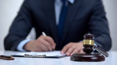 Tecrübeli yargıç evrakları imzalıyor, tokmak masada duruyor, mahkeme salonunda.