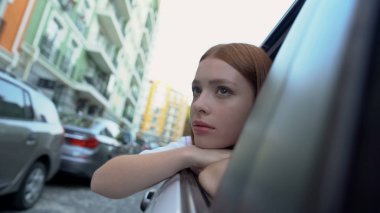 Sad girl saying good bye to native city sitting on back seat of car, relocation clipart