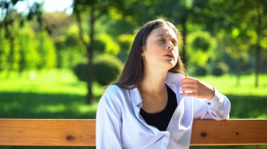 Young woman resting on bench in park suffering from heat and stuffiness, pms clipart
