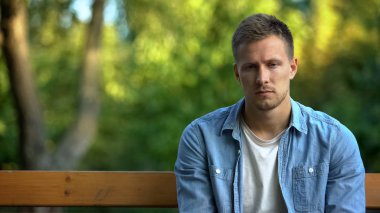 Unhappy young man sitting alone bench thinking problem, trouble depression