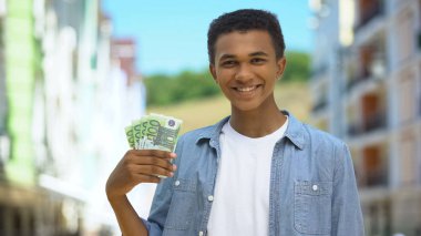 İyi ki melez genç bir erkek. Avro gösteriyor ve gülümsüyor. İlk maaş finansmanı.